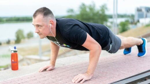 Adult male exercising outdoors performing push-ups with earphones and water bottle., tags: fit - pexel