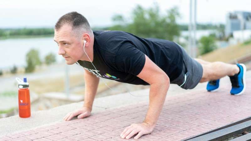 Adult male exercising outdoors performing push-ups with earphones and water bottle., tags: fit - pexel