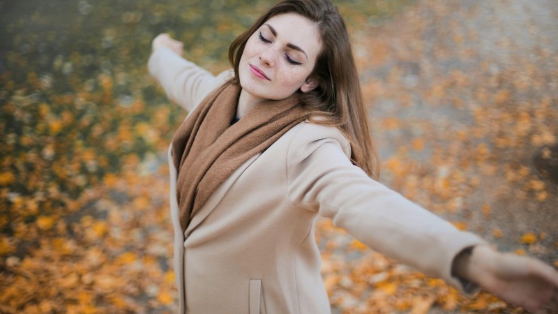 A woman with eyes closed embraces the autumn season amidst fallen leaves., tags: angst en depressie kan - pexel