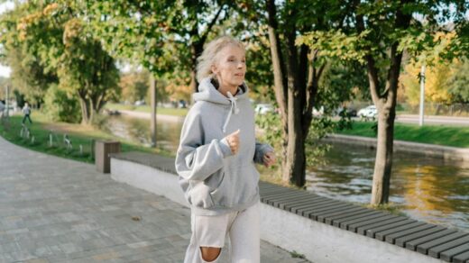 Senior woman in gray hoodie jogging along a park pathway by a canal, embracing an active lifestyle., tags: vrouwen de - pexel