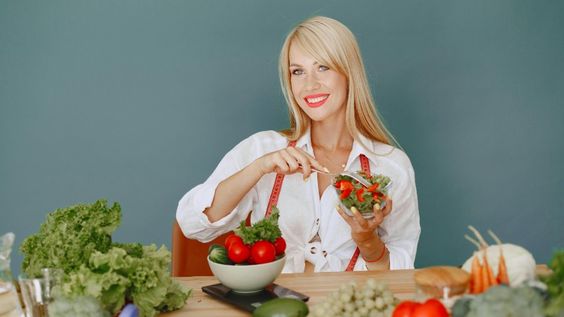 Blonde woman enjoying a fresh salad surrounded by vegetables, promoting healthy eating., tags: een benadering voor - pexel