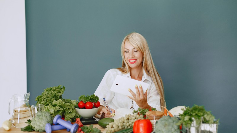 Woman using a tablet surrounded by fresh vegetables at a table, showcasing healthy lifestyle and technology., tags: slimme voeding - pexel